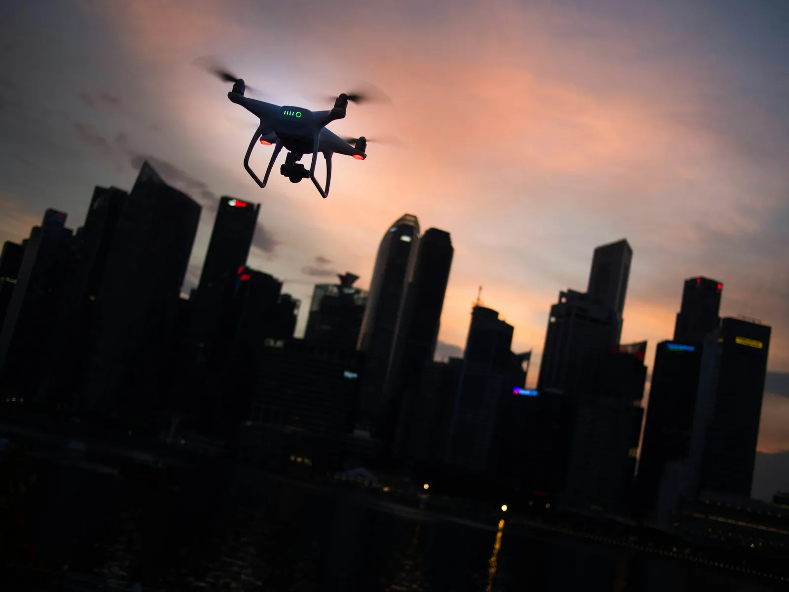 Silhouette of a quadcopter drone hovering against a dusk city skyline
